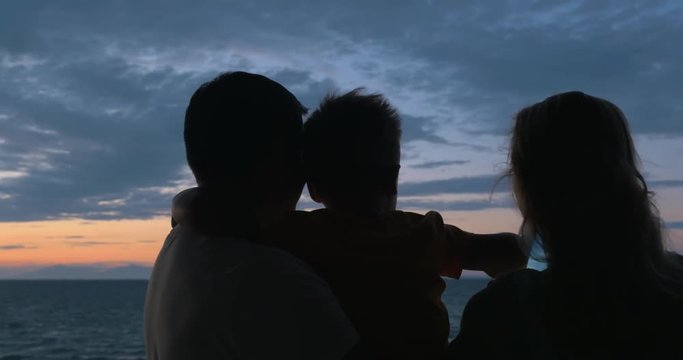 Father stands with son in his arms, and mother is photographed on tablet of sunset and sea in city Perea, Greece. Then mom laughed and kisses his son