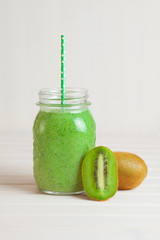 Kiwi smoothie in a jar on a white wooden table.