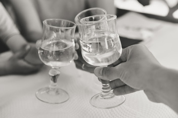Black and white closeup view of human hand holding glass, restaurant light table background
