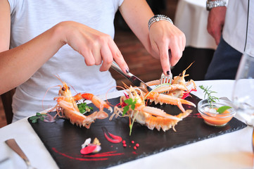 Woman cuts a prawn. The dish in which can be found the three prawns it is very decorated and adorned