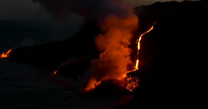 Volcanic Eruption Lava flowing into the water Hawaii at night. 
Steam rising from waves as molten lava flows into ocean waters Big Island Hawaii.