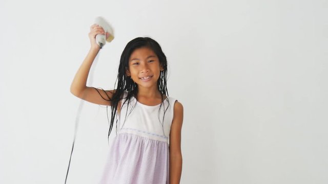 Happy Asian girl dancing while holding hair dryer at home. 