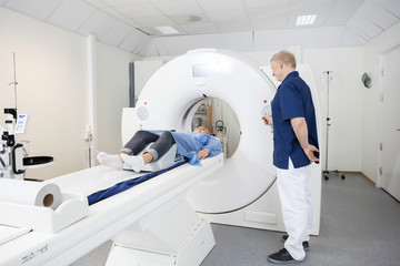 Patient Lying On MRI Machine While Male Doctor Operating It