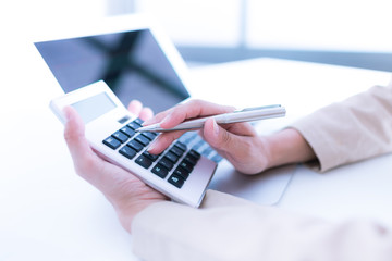 Photo of hands holding pen and pressing calculator buttons. Acco