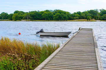 Fototapeta premium Small open motorboat or rowboat moored at wooden pier with archipelago in background. Skavkulla outside Karlskrona in Sweden.