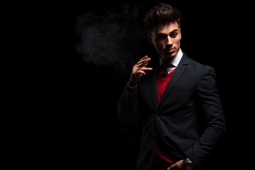 elegant young businessman standing and smoking in studio