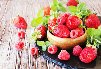 ripe red raspberries and strawberries in wooden bowl, selective focus