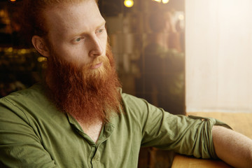Cropped portrait of Caucasian hipster male having long beard and blue eyes sitting at coffee shop...