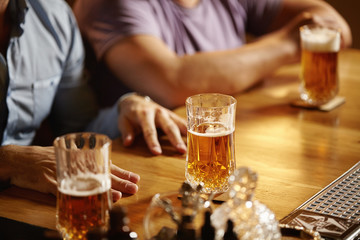 Friendly talk in club. Two happy young men chatting to each other while drinking lager or ale at bar counter. Happy friends having fun at pub watching sport on TV, drinking beer, cheering to team
