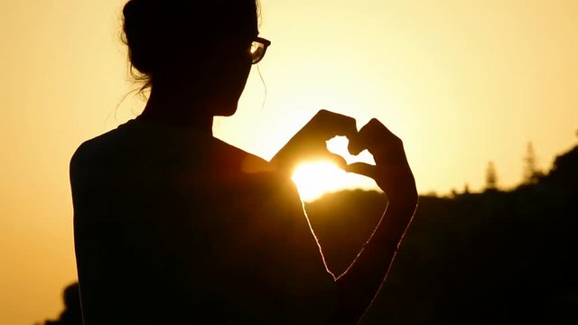 Girl making a heart-shape for the sunset