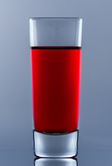 shot glass with red cocktail inside on glass with own reflection