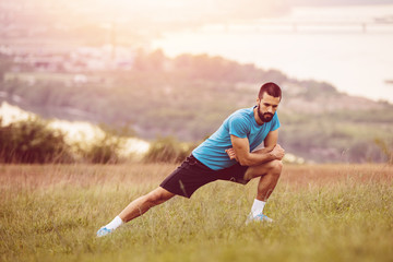 Athletic runner doing stretching exercise, preparing for running in the nature with the city in background. Healthy lifestyle
