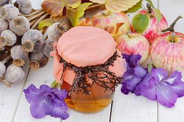 Poppy heads, apples with honey jar on wooden table. 