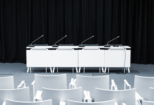 Monochrome Picture Of Empty Press Conference Room With Seats, Stand Table And Microphones