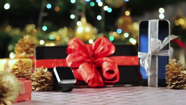 Tablet pc, smartphone and smartwatch with gifts and decorations in front of Christmas tree.