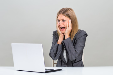 Businesswoman sitting at the table and looking at her laptop in panic.

