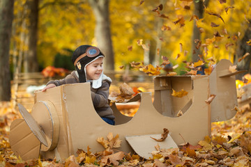Young boy in autumn park in a pasteboard airplane
