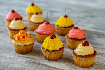 Bright frosted cupcakes. Pastry on gray wooden background. Sweet wonders of cooking. Guess the taste.