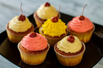 Bright cupcakes with cherries. Desserts on black plate. Surprise your guests. Homemade pastry with icing.