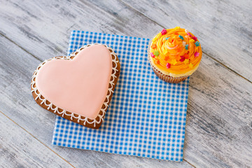 Heart cookie and orange cupcake. Confectionery on napkin. Sweet treats and good feelings. Congratulate your loved ones.