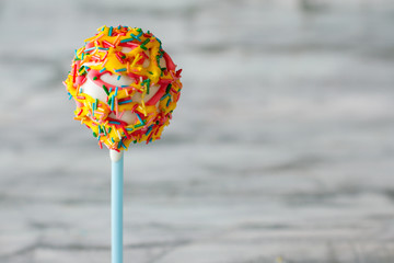 Dessert on stick. White glaze and sprinkles. Try the sweet masterpiece. Candy with soft filling.