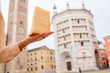 Holding a piece of Parmesan cheese on the Parma main square background in Italy. Parmesan is...