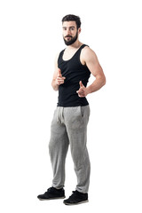 Fototapeta premium Young athlete in tank top pointing fingers at camera. Toned desaturated full body length portrait isolated on white studio background.