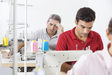 Stressed Tailor With Colleagues Working In Factory