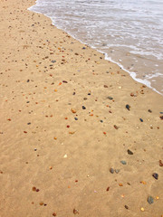 Sand on the beach full of seashells, colorful stones, pebble with waves crashing
