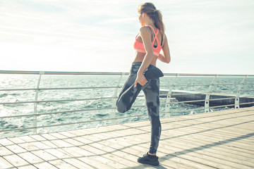 Athletic young woman is stretching her leg on the beach