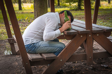 Drunk man sitting on a bench and holding a beer bottle