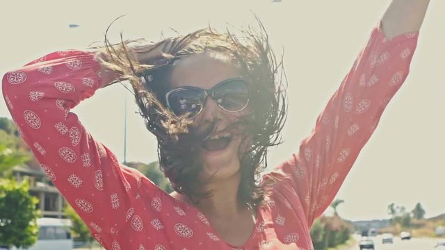 Infinitely happy woman in convertible racing a solar city. Wind fanning her hair. Slow motion.