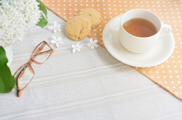 The Time of Tea Break on the table top view. Polka dot tablecloth with cup, cookies, glasses and white flower with copy space