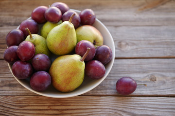 Fototapeta na wymiar Ripe fresh pears and plums in a bowl on a wooden background close up. Autumn harvest of fruit.