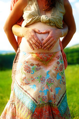 Loving beautiful ethno couple, man makes the heart shape on her pregnant belly.