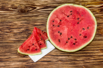 half of watermelon and pieces of watermelon on wooden background