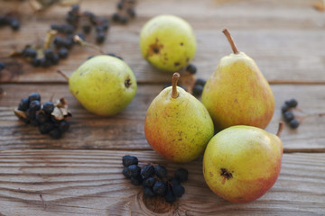 Fresh pears and berries of a black mountain ash on a wooden background close up. Autumn harvest of fruit.