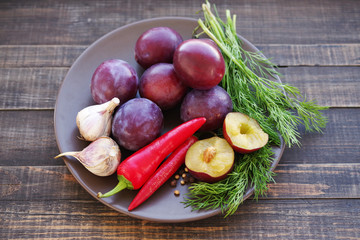 Plums, hot red pepper, garlic, coriander and fennel in a round plate on rustic wood background. Ingredients for preparation of sauce
