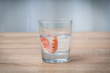 False teeth swim in transparent water glass