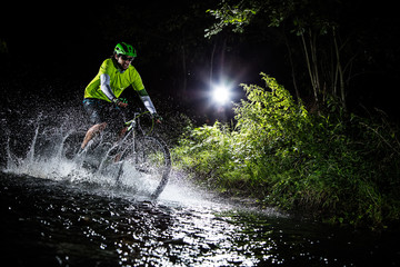 Obraz premium Mountain biker speeding through forest stream. Water splash in freeze motion.