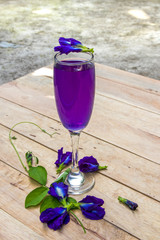Butterfly pea juice in glass on wooden table with flower.