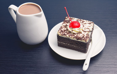 Chocolate cake with cherry and milk jug on black wooden table
