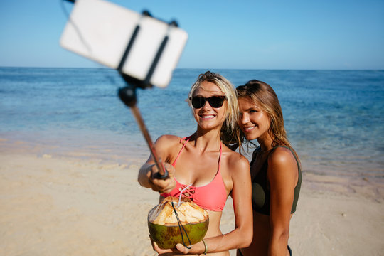 Happy friends taking pictures with selfie stick at the beach