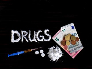 Pile of cocaine drug powder and this powder in drugs word shaped, injection and pills and euro money, coins on banknotes on black background