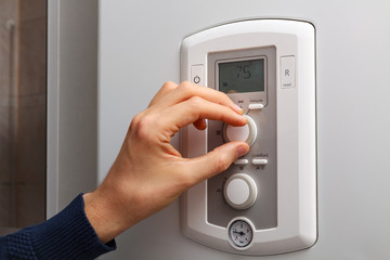 Men hand regulate high temperature on 75 degree in control panel of central heating.