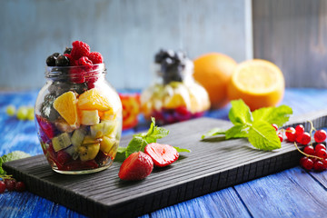 Fresh fruits and berries in glass jar on cutting board