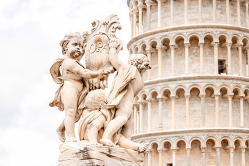 Close-up view on Putti fountain with Pisa leaning tower in Italy
