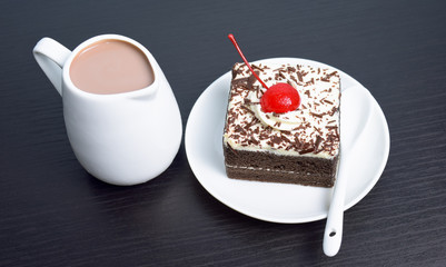 Chocolate cake with cherry and milk jug on black wooden table