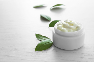 Obraz na płótnie Canvas Facial cream and green leaves on white wooden background