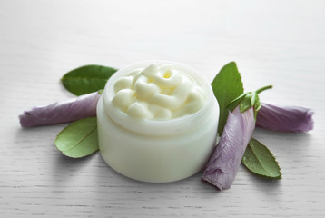 Facial cream and flowers on white wooden background